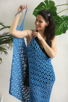 a woman holding onto a blue crocheted shawl in front of a plant