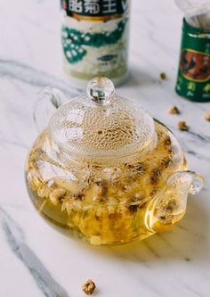 a glass teapot filled with honey sits on a marble surface next to two jars