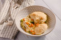 a bowl filled with chicken pot pies next to a fork and napkin on a white table