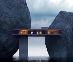 two people standing on a bridge over water with large rocks in the foreground and dark clouds above