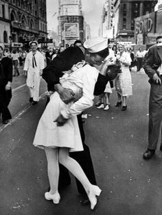 black and white photograph of a man kissing a woman on the street with people in the background