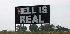 a large sign that says hell is real on the side of a road in front of a farm