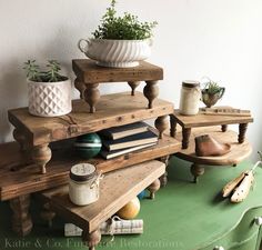 a green table topped with wooden shelves filled with potted plants next to books and vases