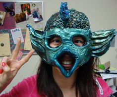 a woman wearing a green mask making the peace sign with her hand and holding up two fingers in front of her face