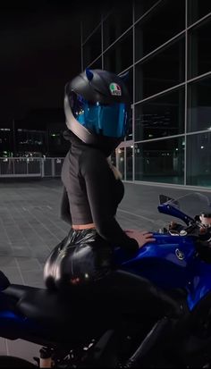 a woman sitting on top of a blue motorcycle in front of a building at night