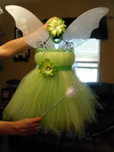 a green fairy dress with white wings and flowers on the top, is being held by someone's hand