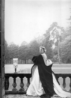 black and white photograph of woman in long dress sitting on stone wall with fountain behind her