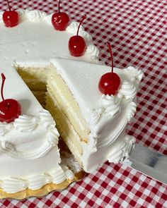 a cake with white frosting and cherries is cut in half on a checkered tablecloth