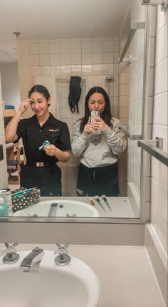 two women are taking pictures in the bathroom mirror while they stand next to each other