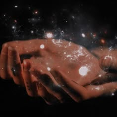 two hands holding each other in the middle of space with stars and dust all around them