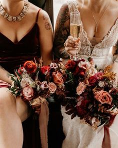 two bridesmaids sitting next to each other holding wine glasses and bouquets in their hands