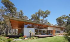 a modern house in the middle of some trees and grass with an open patio area