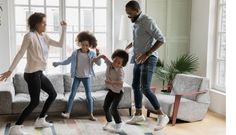 three adults and two children dancing in front of a couch with their feet up on the floor