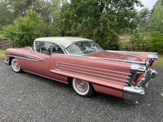 an old pink and white car parked in a parking lot