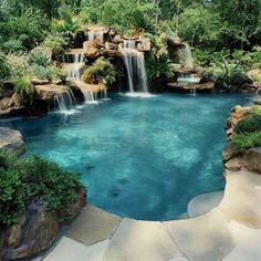 an outdoor swimming pool with waterfall in the middle, surrounded by greenery and rocks