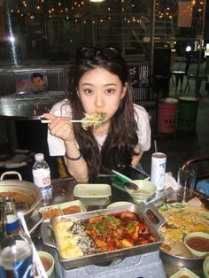 a woman eating food from a tray on top of a table with bowls and spoons