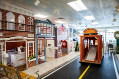 an indoor play area for children with a toy train and slide in the center, surrounded by fake buildings