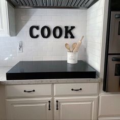 a kitchen with white cabinets and black counter tops that says cook on the wall above the stove