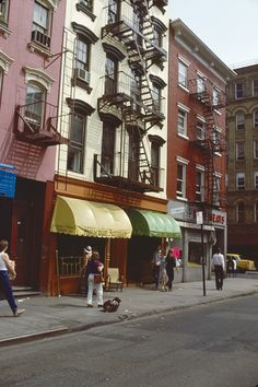 people are walking down the street in front of tall buildings with fire escapes on them