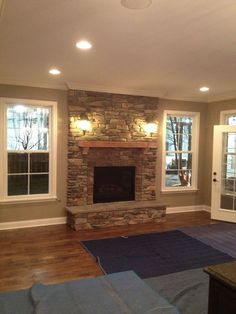 an empty living room with a stone fireplace and windows in the wall, blue rugs on the floor