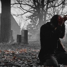 a woman sitting on the ground in front of a cemetery with her hands to her face