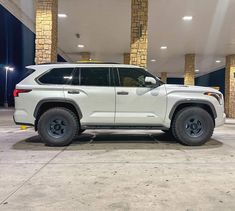 a white toyota suv parked in a parking lot next to two tall pillars with lights on