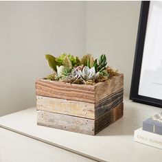 a wooden planter with succulents sits on a desk next to a book