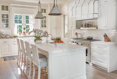 a large kitchen with white cabinets and an island in the middle, surrounded by chairs