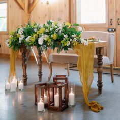 an arrangement of flowers and candles on the floor in front of a table with chairs