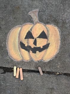 some chalk crayons are laying on the ground next to a drawing of a jack - o'- lantern