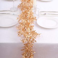 the table is set with white plates, silverware and gold leafy garland on it