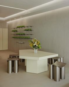 a white table surrounded by metal stools and vase with flowers on it in an empty room