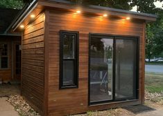 a small wooden building with windows and lights on the outside, in front of a house