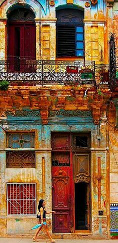 two people walking down the street in front of an old building with doors and windows