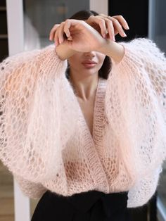 a woman wearing a pink sweater and black pants with her hands on her head, posing in front of a window