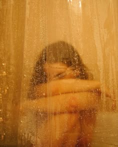 a woman sitting in front of a window covered in water droplets and looking at her reflection