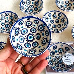 a hand is holding a blue and white bowl in front of several other bowls on the table