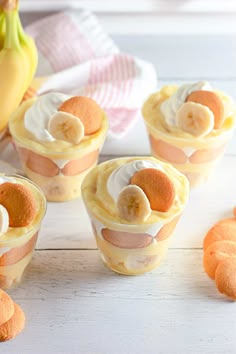 small desserts with bananas and cream in them on a white wooden table next to fruit