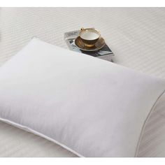 a white pillow sitting on top of a bed next to a cup and saucer