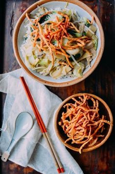 two bowls filled with noodles and vegetables next to chopsticks on a wooden table