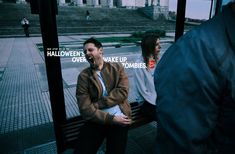 a man and woman sitting on a bench in front of a building with halloween's over, wake up zombies written on it