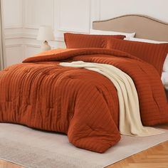 a bed with an orange comforter on top of it and a white rug in front of it