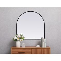 a mirror sitting on top of a dresser next to a vase with flowers in it