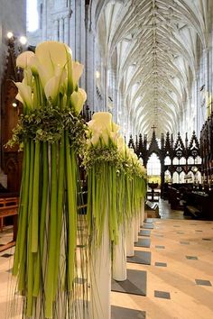 two tall white vases filled with flowers on top of a tiled floor in a cathedral