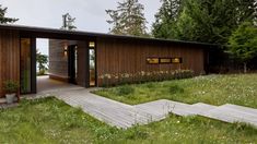 a wooden house sitting on top of a lush green hillside next to trees and grass