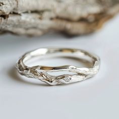 a silver ring sitting on top of a piece of driftwood next to a tree branch