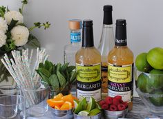 two bottles of wine and some fruit on a table with paper straws, limes, raspberries