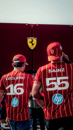 two men in matching red shirts are walking towards a large truck with the number 65 on it