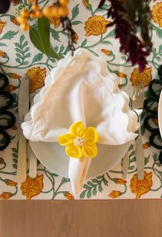 a white plate topped with a yellow flower on top of a table next to utensils