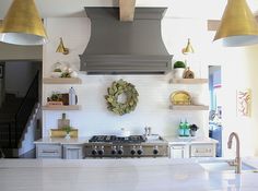 a kitchen with white counter tops and gold pendant lights hanging from the ceiling over the stove